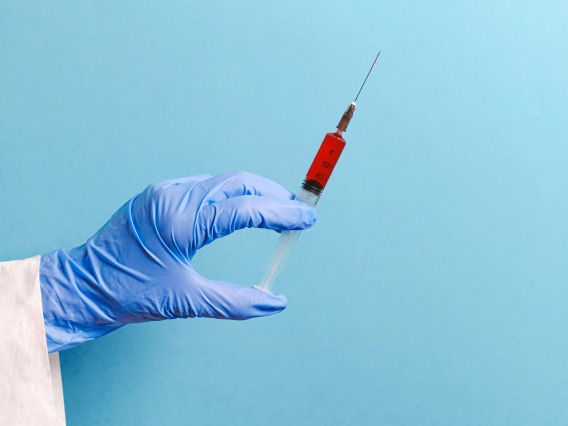 Gloved hand holding a vaccine against a light blue background 