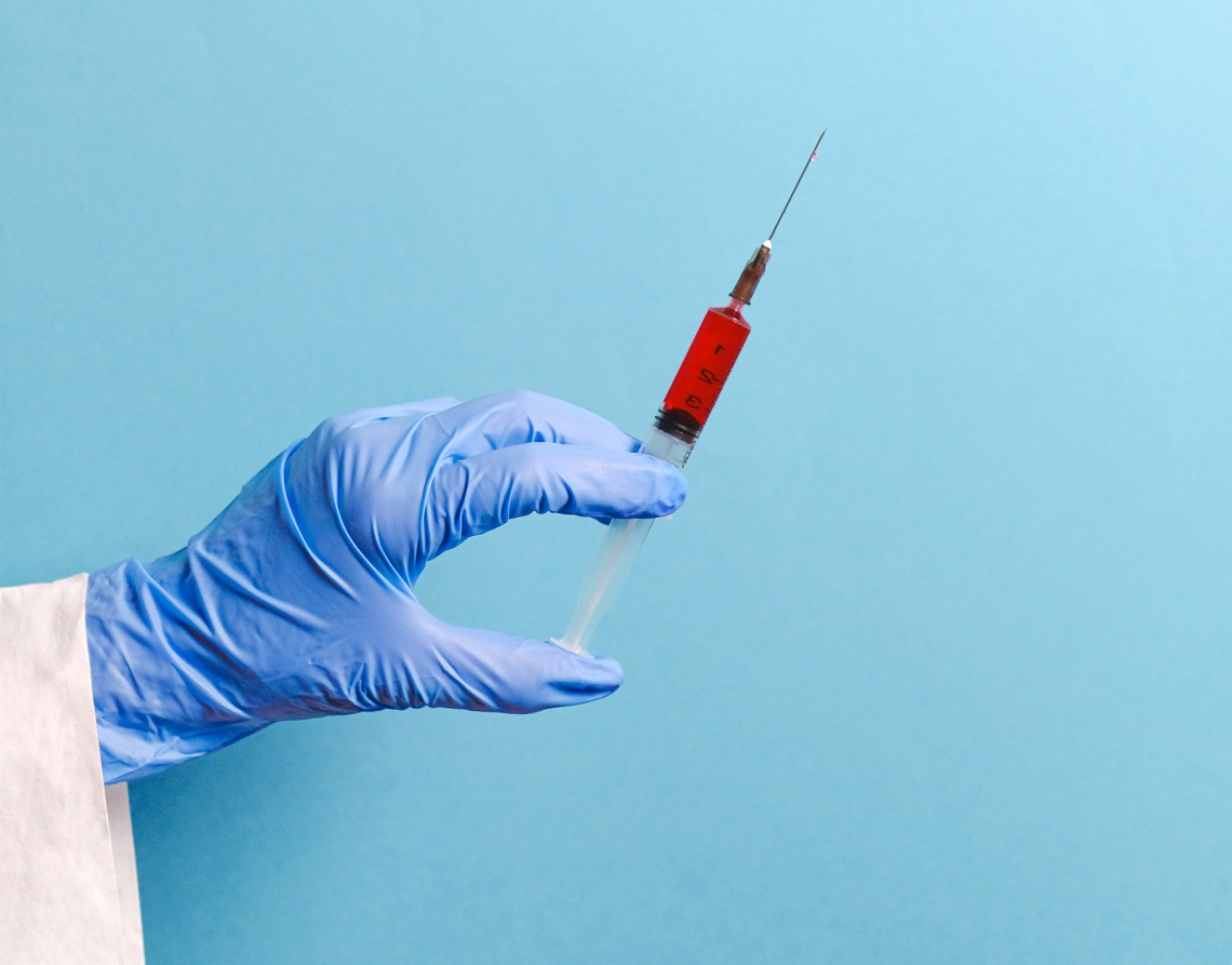 Gloved hand holding a vaccine against a light blue background 